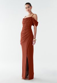 Rostfarbiges schulterfreies Kleid mit tailliertem Oberteil, drapiertem Stoff, seitlichem Schlitz und dünnen Trägern, mit einer glatten, fließenden Textur.
