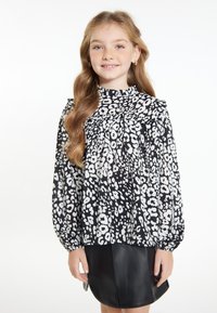 Bluse med sort og hvidt dyreprint, med samlet hals, lange puffærmer og løs pasform, parret med en sort lædernederdel.
