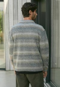Hallide triibuline kudum sweater, millel on kaelusega kaelus, pehme tekstuur ja soonikserv, kombineeritud tumede pükstega.
