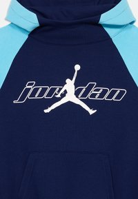 Granatowa i jasnoniebieska bluza z kapturem z białym logo Jumpman i napisem "jordan" z przodu, z kieszenią kangurzą poniżej wzoru.