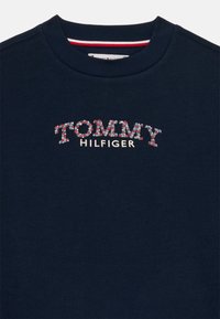 Námornícka modrá mikina vyrobená z mäkkého materiálu, s mnohobarevnou výšivkou loga "TOMMY HILFIGER" a rebrovaným okrajom okolo krku.