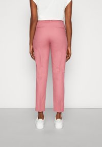 Rosa skräddarsydda byxor med slim fit, som har en mjuk textur, två bakfickor och är kombinerade med vita sneakers.