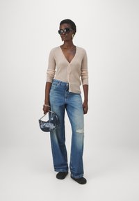 Ljusbeige ribbad cardigan, blå vida jeans med slitna detaljer, svart väska med kedjesnodd och svarta solglasögon.