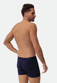 Boxer de algodón azul marino con una banda elástica con logo, de ajuste ceñido y textura suave, vistos desde atrás.