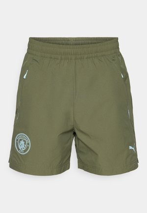 Oliven grønne treningsshorts med elastisk midje, Manchester City-logo på venstre bein, Puma-logo på høyre bein, og glidelåslommer på siden.