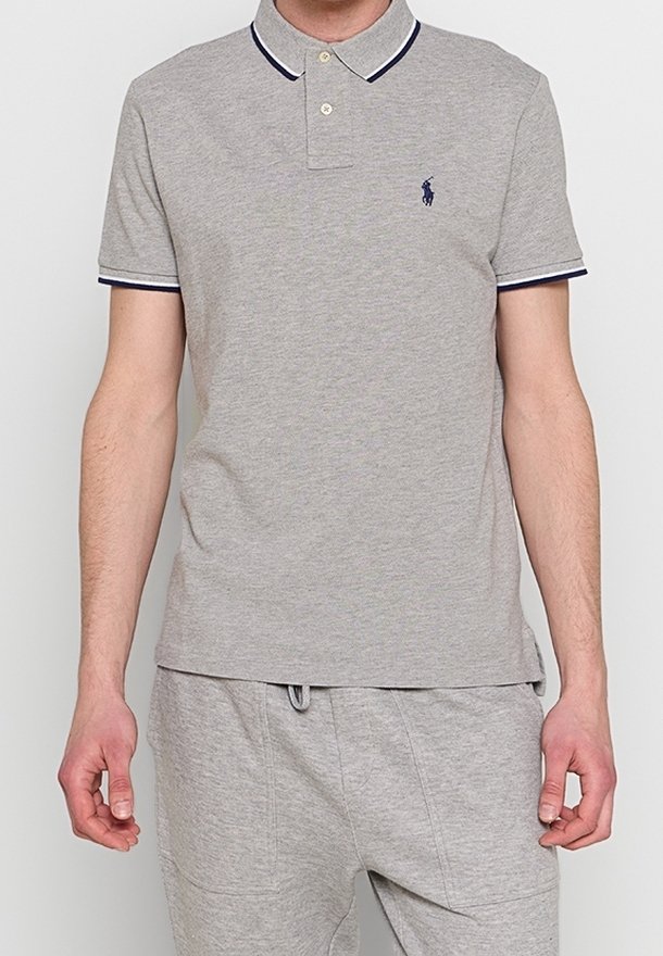 Homme portant un polo gris clair à manches courtes avec une bordure foncée au col et aux manches, associé à un pantalon gris clair assorti.