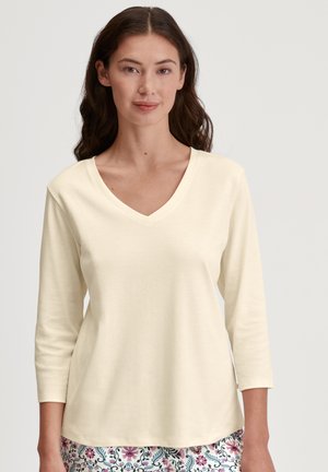 Maglietta a maniche lunghe color crema con scollo a V in un tessuto morbido, caratterizzata da una vestibilità rilassata e una superficie liscia. I motivi sono visibili sul fondo.