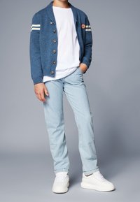 Sininen neulecardigan, jossa on valkoiset raidat ja puunapit, käytetty valkoisen t-paidan päällä kevyiden sinivalkoisten raidallisten housujen kanssa ja valkoisten lenkkareiden kera.