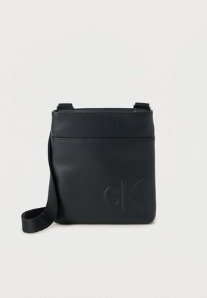 Juoda odinė kryžminio nešiojimo rankinė su įspaustu "cK" logotipu, lygiu paviršiumi, reguliuojama rankena ir priekinė kišenė papildomam daiktų laikymui.