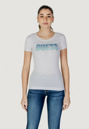 Camiseta blanca de manga corta con un logotipo "GUESS" brillante en gradiente azul, diseño ajustado, textura suave, combinada con jeans azules.