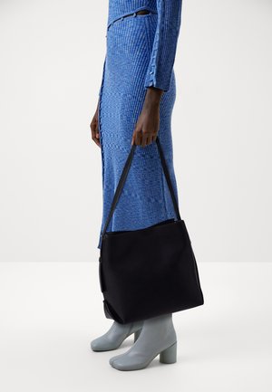 Sac fourre-tout noir avec deux poignées, en tissu lisse et à la forme structurée, assorti à une longue robe bleue côtelée et des bottes à talons bleu clair.