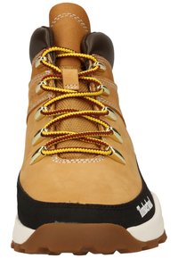 Botte de randonnée en cuir marron avec des lacets jaunes et bordeaux, œillets en métal, col rembourré et semelle en caoutchouc noir. Présente des coutures contrastantes.