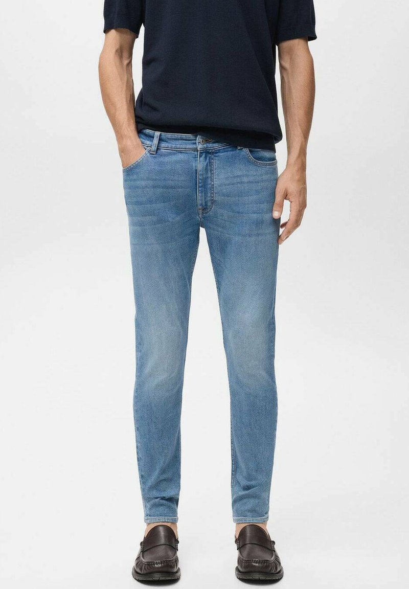 Jeans de mezclilla azul claro con corte slim, que cuentan con bolsillos delanteros y una cinturilla. Llevados con una camisa oscura de manga corta y zapatos.