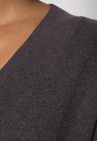 V-Ausschnitt-Pullover aus dunkelgrauem Strickstoff, mit strukturiertem Rippenmuster entlang des Ausschnitts und glatter Oberflächenstruktur, die ein weiches Gefühl zeigt.