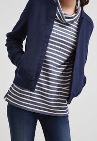 Marinblå dragkedjetröja över en grå och vit randig topp. Jackan har en avslappnad passform med ribbade ärmslut, och toppen har en cowl-hals.