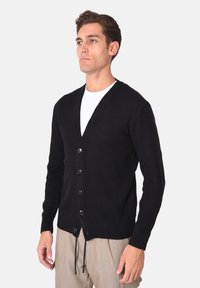 Cardigan nero a costine con scollatura a V, presenta cinque bottoni, maniche lunghe e coulisse sull'orlo. Tessuto a maglia strutturato.