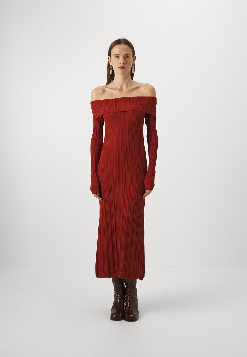 Rochie maxi cu umerii descoperiți, din material texturat, într-o nuanță roșie închisă. Mâneci lungi, ajustate, cu o siluetă modernă, asortată cu cizme maro până la genunchi.