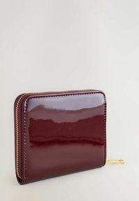 Portafoglio in pelle verniciata bordeaux con zip e tirante dorati. Presenta una superficie liscia e una forma rettangolare con dettagli di cucitura curati.