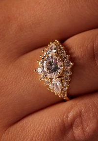 Gouden ring met een centrale ronde diamant, omringd door peren-vormige en kleinere ronde stenen, met een gestructureerde zetting en parelachtige accenten.