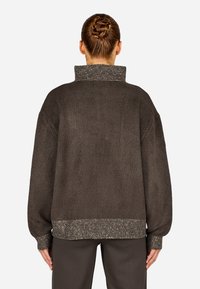 Prehnutý hnedý sveter s vysokým, textúrovaným golierom a rebrovaným, kontrastným lemom. Mäkká tkanina s voľným strihom a dlhými rukávmi.