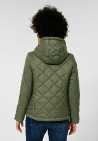 Vihreä tikattu takki hupulla, jossa on sileä rakenne, viistot saumat ja helma ulottuu vyötärölle. Päällä siniset farkut.