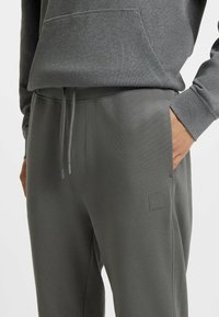 Gray sweatpants with a textured finish, featuring an elastic waistband, drawstring, and a logo patch on the leg.