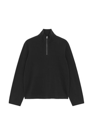 Juodas ilgomis rankovėmis megztinis su ribsniuotu aukštu apykakliu ir pusiau užtrauktuku priekyje centre.