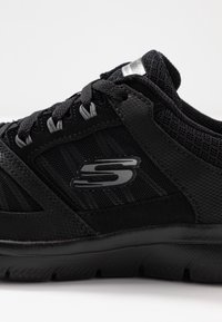 Černá sportovní bota vyrobená z prodyšného a syntetického materiálu. Obsahuje šedé akcenty, texturovaný povrch a výrazné stříbrné logo na boku.