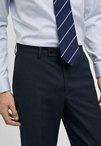 Pantaloni de ceremonie navy dintr-un material neted, având un buzunar frontal cu nasture, asortați cu o cămașă de ceremonie bleu deschis și o cravată cu dungi.