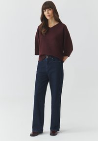 Bordeaux, oversized V-hals trui met ellebooglange mouwen, gecombineerd met high-waisted, straight-leg, donkerblauwe jeans en bordeaux schoenen.