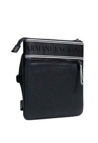 Bolso bandolera negro con textura, con un bolsillo frontal con cremallera y una correa en blanco y negro con la marca "Armani Exchange".