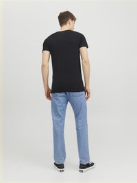 Schwarzes kurzärmliges T-Shirt, getragen mit hellblauen Jeans und schwarzen Sneakers, von hinten gegen einen schlichten hellen Hintergrund betrachtet.