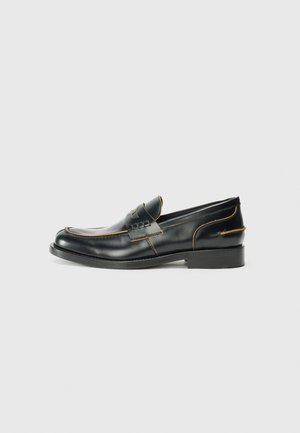 Mocassins en cuir noir au design épuré, avec des coutures discrètes et un talon bas, présentés sur un fond blanc uni.