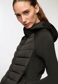 Czarna kurtka ocieplana z pikowanym przodem, gładkimi rękawami i kapturem. Zamek błyskawiczny z przodu z eleganckimi detalami, idealna do noszenia na cebulkę.