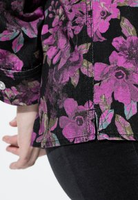 Camicia di tessuto nero con un vivace motivo floreale rosa, superficie testurizzata e dettagli delle cuciture visibili. Accenti a bottoni ai polsi.