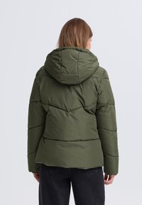 Grüne gesteppte Jacke mit Kapuze, Chevron-Steppung und strukturierter Oberfläche, designed für Wärme und Komfort.