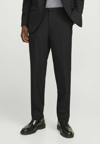 Czarne dopasowane spodnie o prostym kroju, z plisowanym przodem i subtelnym połyskiem, w połączeniu z eleganckimi czarnymi oksfordami.