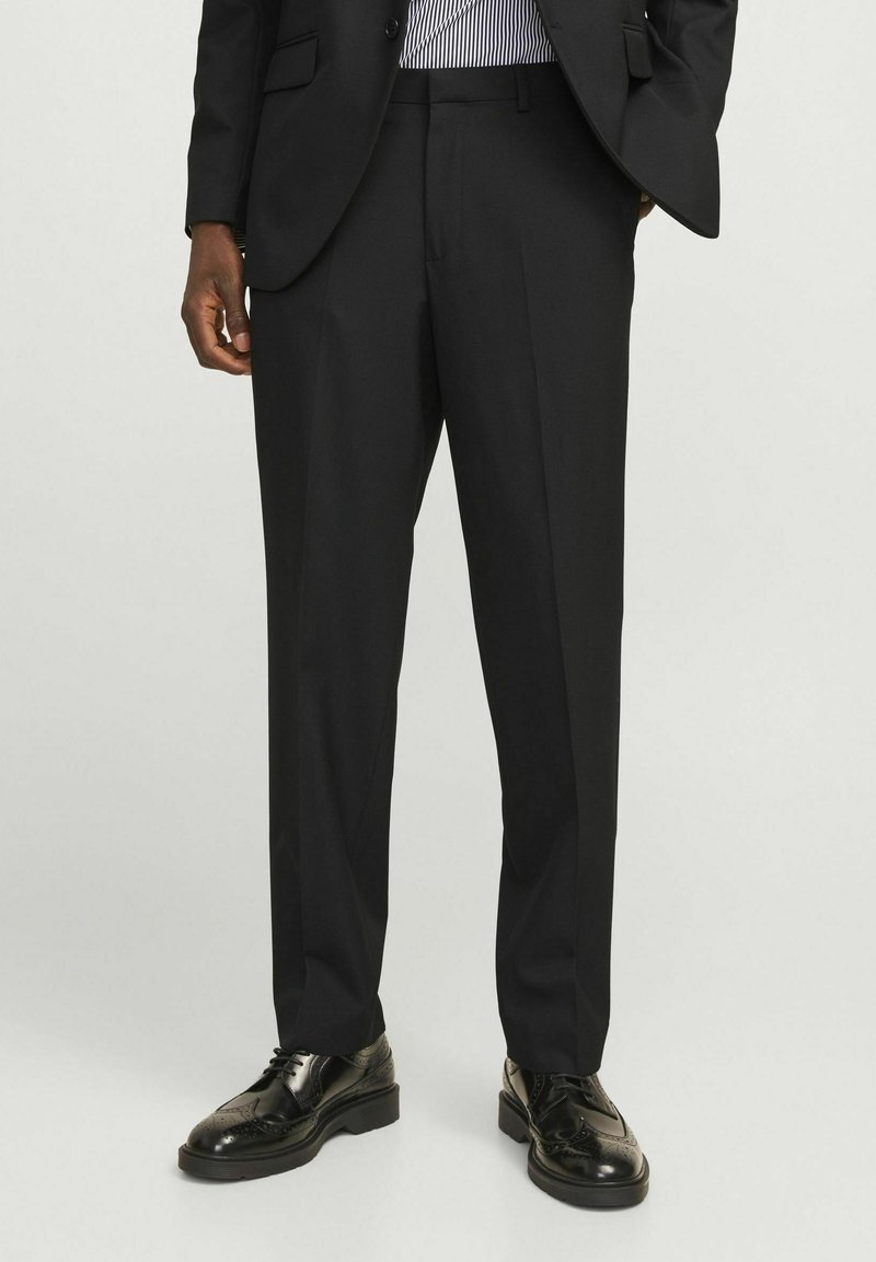 Czarne dopasowane spodnie o prostym kroju, z plisowanym przodem i subtelnym połyskiem, w połączeniu z eleganckimi czarnymi oksfordami.