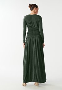 Dlhé zelené šaty z jemného materiálu s priliehavým korzetom a zberaním na chrbte, prechádzajúce do plnej sukne, s dlhými rukávmi a zapínaním na chrbte.