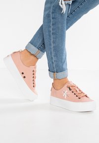 Rosa canvas sneakers med en vit plattformssula, med rund tå, sex ögla, och en dekorativ logotyp nära hälen. Uppvikt muddjeans i denim.