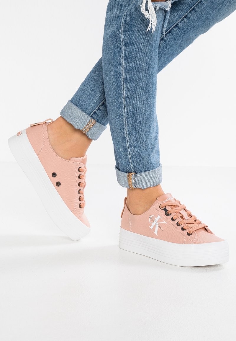 Rosa canvas sneakers med en vit plattformssula, med rund tå, sex ögla, och en dekorativ logotyp nära hälen. Uppvikt muddjeans i denim.