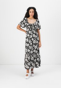 Sort blomster maxi kjole med korte pufærmer, firkantet halsudskæring, indsnævret talje og flagrende nederdel. Har hvid blomsterprint og letvægtigt stof.