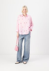 Light pink button-up shirt with red heart embroidery, paired with wide-leg denim jeans featuring heart outlines. Accessorized with a pink handbag.