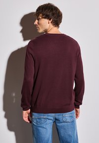 Pull en tricot bordeaux à manches longues, col et ourlet côtelés, associé à un jean en denim bleu clair, vu de l'arrière.