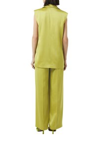 Limonengrünes ärmelloses Oberteil mit Kragen, kombiniert mit passenden weit geschnittenen Hosen. Glatte Textur mit einem minimalistischen Design.
