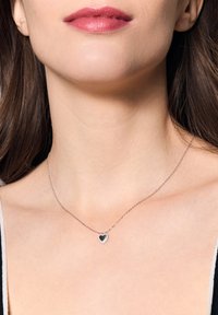 Srebrny naszyjnik z łańcuszka z zawieszką w kształcie serca, z czarnym środkiem i halo z małych białych kamieni wokół.