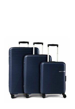 Trois valises rigides bleu marine de tailles différentes avec des poignées télescopiques déployées et quatre roulettes pivotantes chacune, disposées côte à côte sur fond blanc.