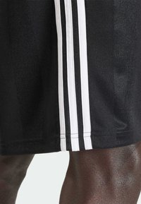 Fekete sportnadrág, oldalán három fehér függőleges csíkkal; texturált anyag sima felülettel, varrott szegéllyel.