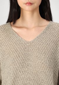 Maglione beige a scollo a V con un motivo in maglia testurizzata e una vestibilità rilassata, con cuciture visibili e una tonalità naturale e discreta.