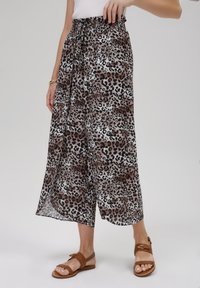 Pantalons larges à imprimé léopard en tissu léger avec une taille élastique. Palette de couleurs brun, noir et crème. Sandales plates portées.